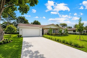 A single-story house with a garage, surrounded by a well-maintained lawn and trees. - Coral Springs Oasis Retreat (Coral Springs)