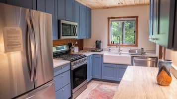 A modern kitchen with stainless steel appliances, blue cabinets, and a window providing a view of greenery.