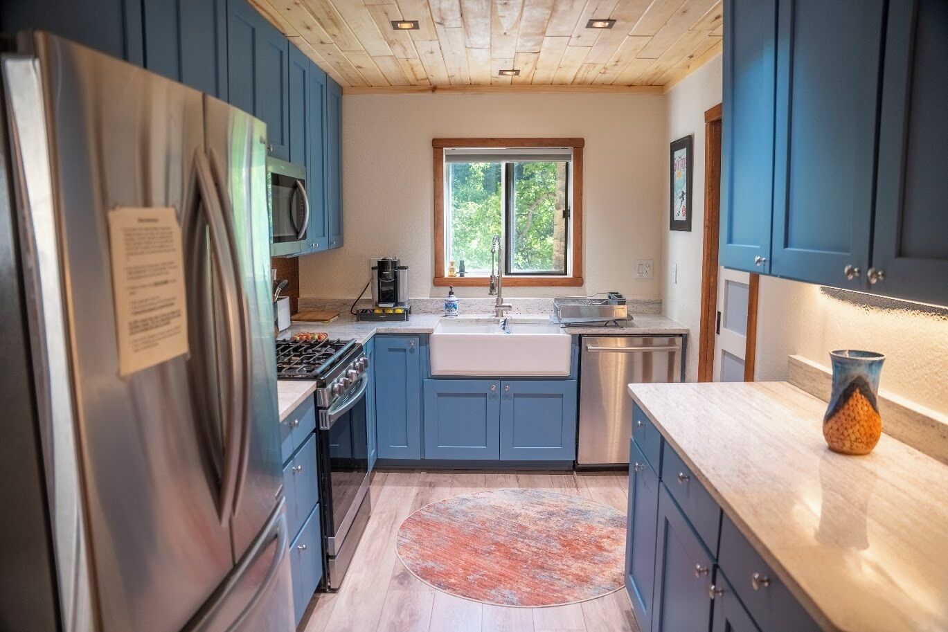 A modern kitchen with blue cabinets, stainless steel appliances, and a large window.
