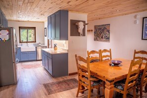 Une cuisine moderne avec des meubles gris, une table à manger en bois avec six chaises et une décoration représentant une tête de taureau accrochée au mur.