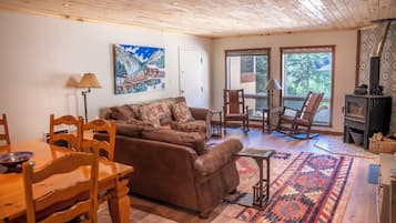 A cozy living room with a brown sofa, wooden chairs, a dining table, and a fireplace.