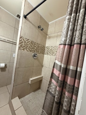 A shower with a tiled wall, a showerhead, and a curtain.