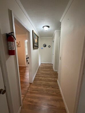 A hallway with wooden flooring, white walls, a fire extinguisher, and a ceiling light fixture.