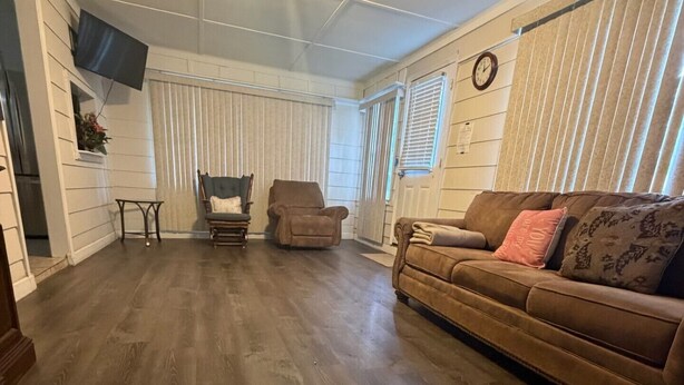 A living room with a wooden floor, a brown sofa, two armchairs, and a TV mounted on the wall. - Tranquil 3-bedroom house with AC in charming Eastman (Eastman)