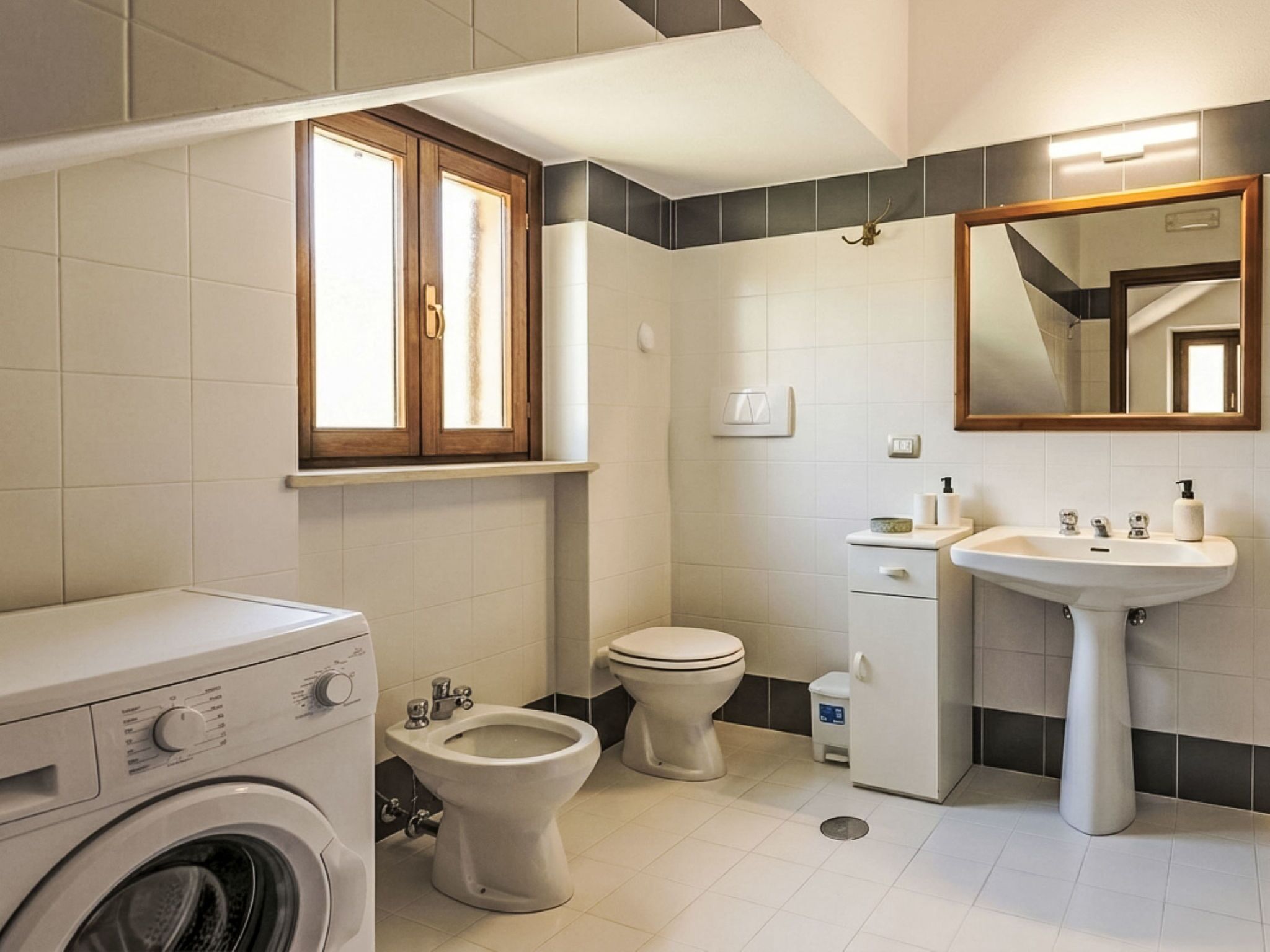A bathroom with a washing machine, bidet, toilet, sink, and a mirror.