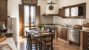 Een keuken met houten kastjes, een eettafel met stoelen, een fornuis en een koelkast.