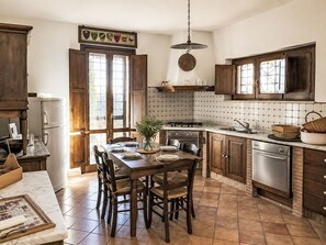 A kitchen with wooden cabinets, a dining table with chairs, a stove, and a refrigerator. - Le More by Interhome (Penna in Teverina)