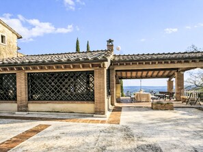 A building with a tiled roof, a covered patio area with outdoor seating, and a view of the landscape. - Le More by Interhome (Penna in Teverina)