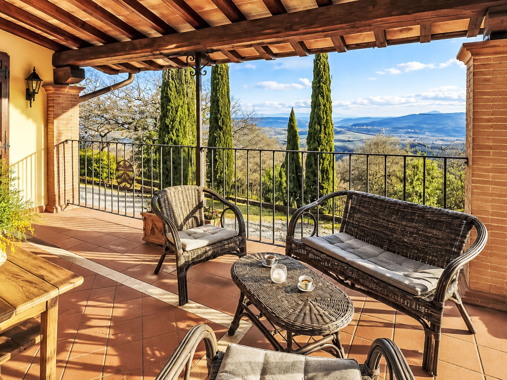 A covered patio with wicker furniture, a view of the countryside, and a brick wall.