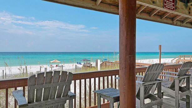 Eine Holzterrasse mit Adirondack-Stühlen mit Blick auf einen Strand.