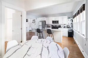 A modern kitchen with white cabinets, a central island, and a dining area with a marble table. - 9 BR Movie Theater Duplex Near Cleveland Clinic! (Cleveland)