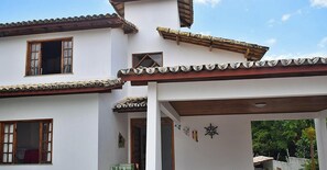 A two-story building with a tiled roof, wooden window frames, and a small balcony. - Casa Porto Seguro Village - PS-BA (Porto Seguro)