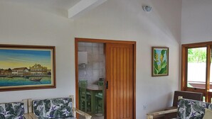 A room with a view of a body of water, a dining area with green chairs, and a wooden door leading to a kitchen. - Casa Porto Seguro Village - PS-BA (Porto Seguro)