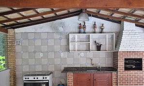 A kitchen with a gas stove, a brick oven, and a hanging fan. - Casa Porto Seguro Village - PS-BA (Porto Seguro)