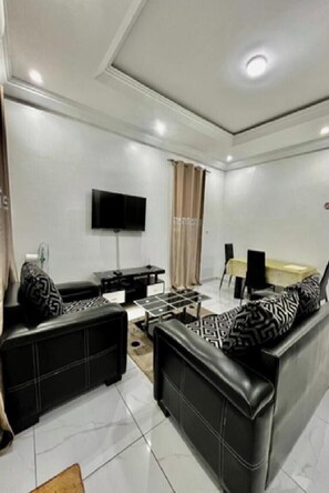 A modern living room with a flat-screen TV, a sofa set, a coffee table, and a dining area with chairs.