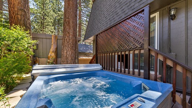 Un jacuzzi con cubierta de madera y una casa al fondo.