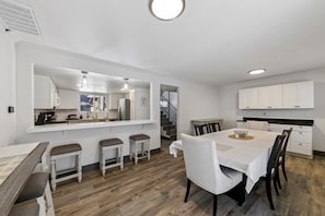 Eine moderne Küche mit weißen Schränken, ein Essbereich mit Holztisch und -stühlen sowie eine Treppe zu einer weiteren Ebene.