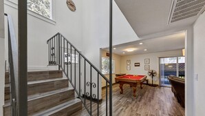 Una escalera de madera con barandilla de metal que conduce a una habitación con mesa de billar y futbolín.