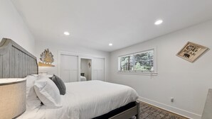 Un dormitorio con una cama, una mesita de noche, una lámpara, una ventana y un adorno de pared.