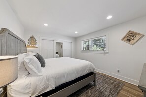Ein Schlafzimmer mit Bett, Nachttisch, Lampe, Fenster und Wandbild.