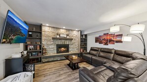 Una sala de estar con chimenea de piedra, sofá de cuero, televisor de pantalla plana y cuadros en la pared.
