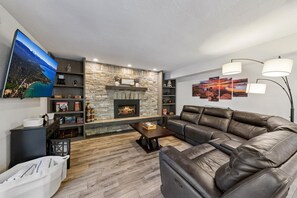 Ein Wohnzimmer mit Kamin aus Stein, einer Ledersofa, einem Flachbildfernseher und Wandbildern.