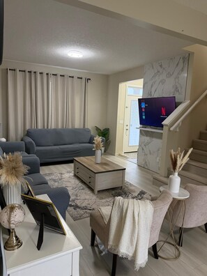 A living room with a grey sofa, a coffee table, a TV, and a staircase. - Stylish Family Home | 3 Bedrooms | Close to Airport & City (Calgary)