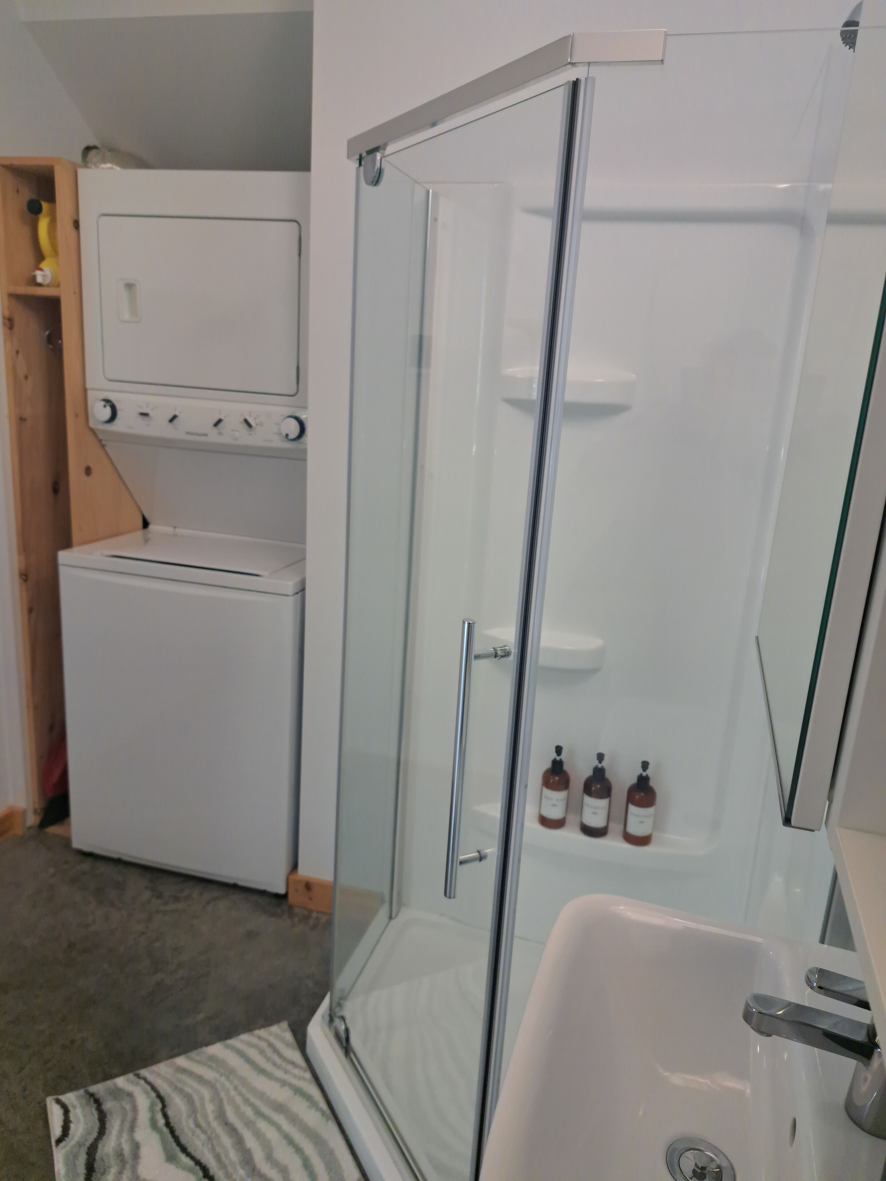 A bathroom with a glass-enclosed shower, a white sink, and a built-in washing machine.