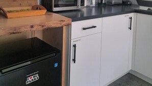 Uma cozinha compacta com armários brancos, micro-ondas, cafeteira e uma geladeira pequena.