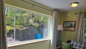 Um quarto com uma janela grande, um abajur, um sofá e um quadro na parede.