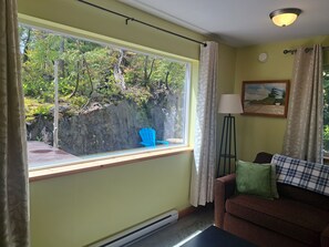 Una habitación con un ventanal grande, una lámpara de pie, un sofá y un cuadro en la pared.