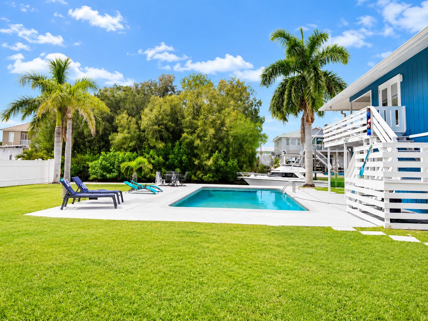 A swimming pool with lounge chairs, palm trees, and a blue building with a deck.