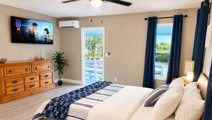 Un dormitorio con cama, cómoda, televisor, aire acondicionado y vista al exterior.