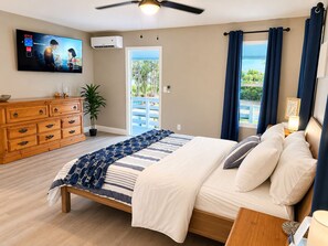 A bedroom with a bed, a dresser, a TV, an air conditioner, and a view of the outdoors.