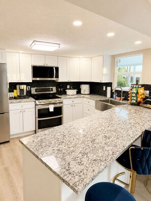 A modern kitchen with white cabinets, a granite countertop, stainless steel appliances, and a view of the outdoors.