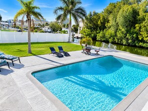 Una piscina con sillas de descanso y una mesa, rodeada por una cerca blanca y palmeras.