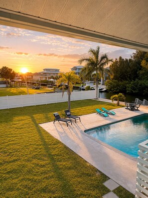 A pool area with lounge chairs, a small pool, and a view of the sunset.