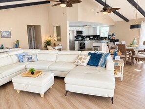 Un salón amplio con un sofá seccional blanco grande, una mesa de centro de madera y una zona de comedor con una mesa y sillas blancas.