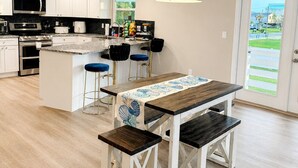 Una cocina moderna con armarios blancos, una isla central, taburetes de bar y una lámpara colgante.