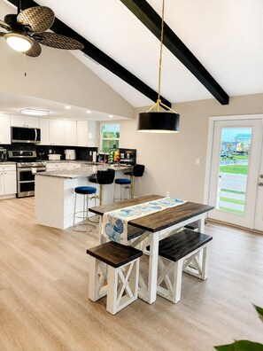 A modern kitchen with white cabinets, a central island, bar stools, and a hanging pendant light.
