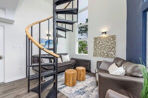 Ein modernes Wohnzimmer mit Wendeltreppe, einer Couch, zwei runden Holzschemeln und einem großen abstrakten Wandkunstwerk.