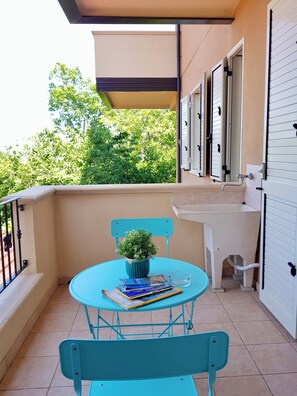 Ein Balkon mit Tisch, Stühlen, einem Blumentopf und einem Fenster mit Rollläden.