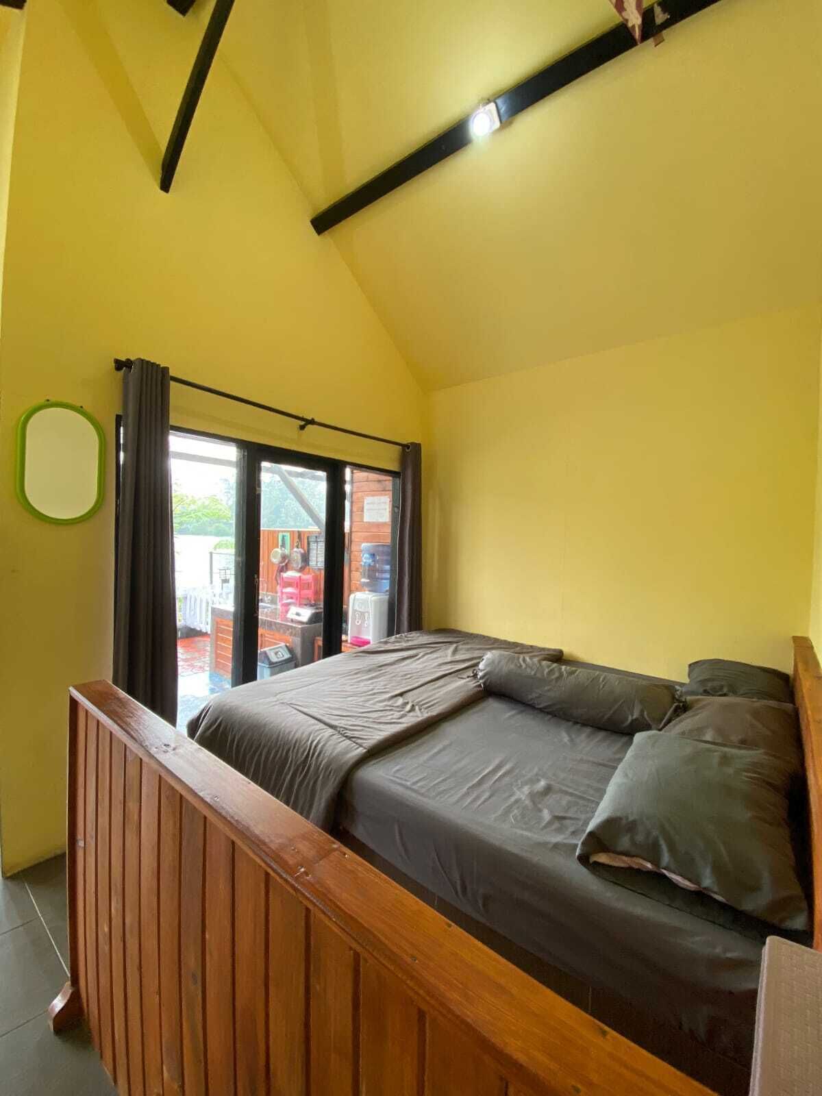 A bedroom with a bed, wooden headboard, a window with curtains, and a view of the outside.