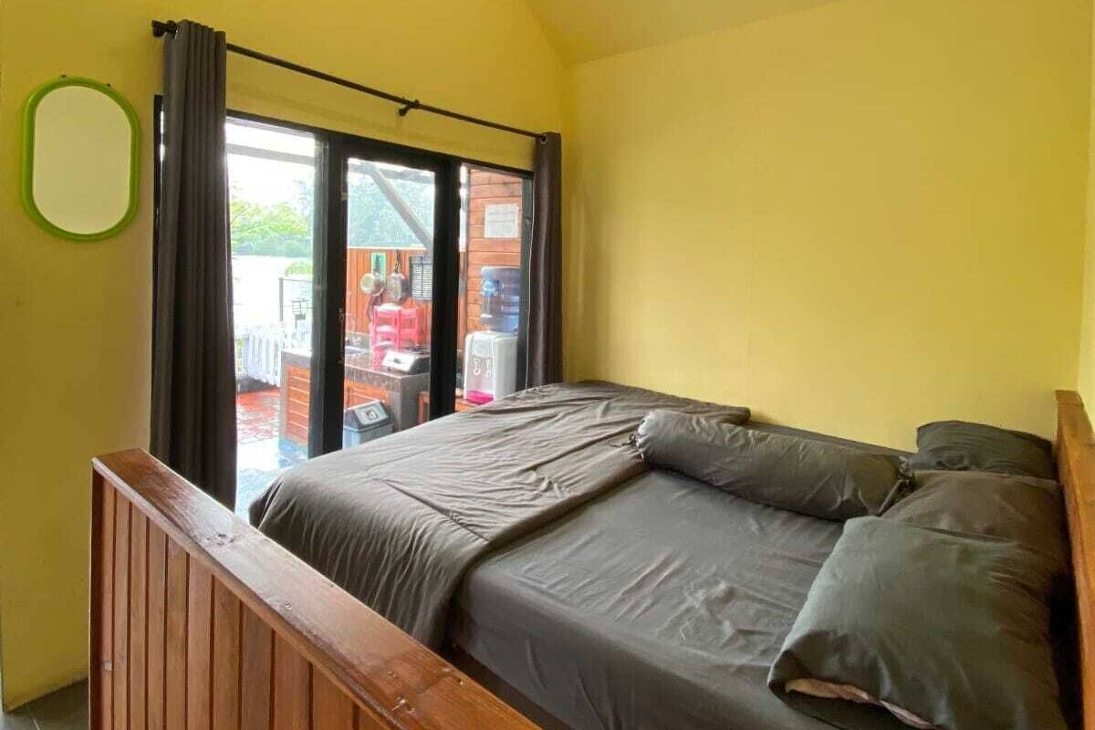A bedroom with a bed, wooden headboard, a window with curtains, and a view of the outside.