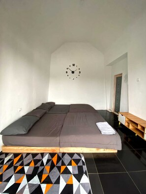 A room with a bed, a clock on the wall, and a geometric-patterned rug. - Cozzy Boemi Chips Pangalengan (BANDUNG)