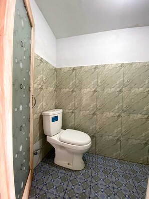 A small bathroom with a toilet, tiled walls, and a patterned floor. - Cozzy Boemi Chips Pangalengan (BANDUNG)