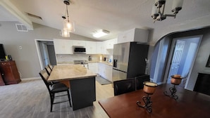 A modern kitchen with white cabinets, a large island, and a dining area with a wooden table and chairs.