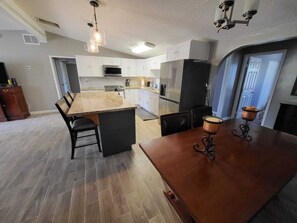 A modern kitchen with white cabinets, a large island, and a dining area with a wooden table and chairs.