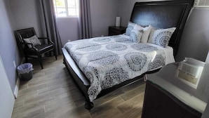 A bedroom with a bed, a chair, a desk, a ceiling fan, and a window.