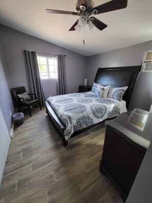 A bedroom with a bed, a chair, a desk, a ceiling fan, and a window.
